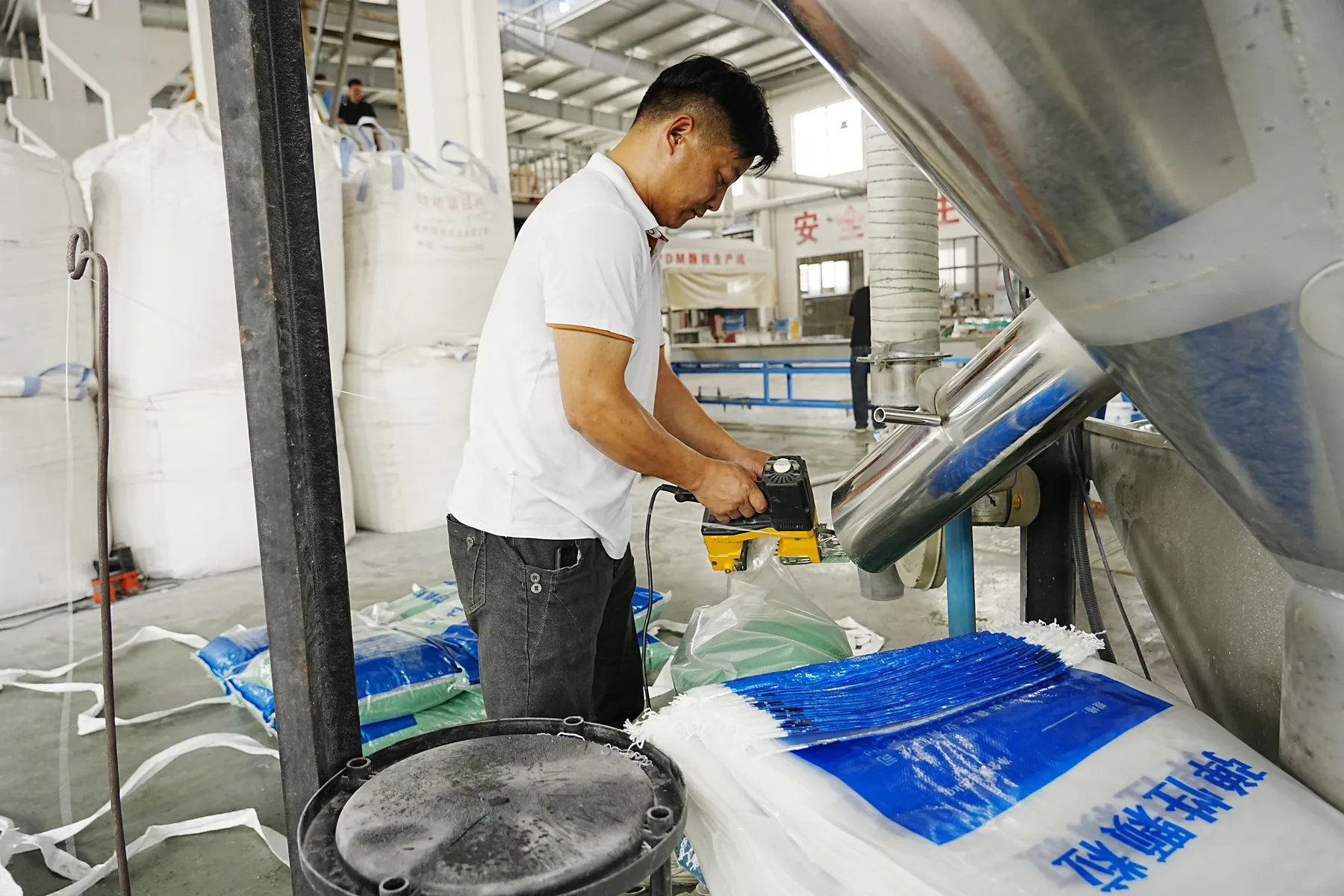 Operator sealing a finished-material bag beside production equipment